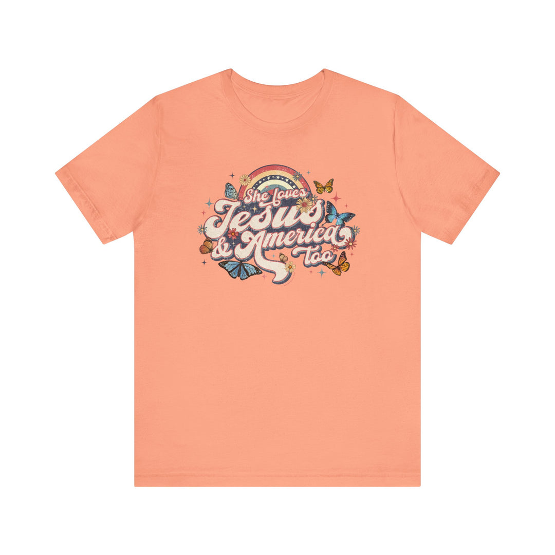 A pink She Loves Jesus and America Tee with a graphic design of butterflies and flowers on soft cotton. Unisex jersey shirt with ribbed knit collars, taping on shoulders, and tear-away label.