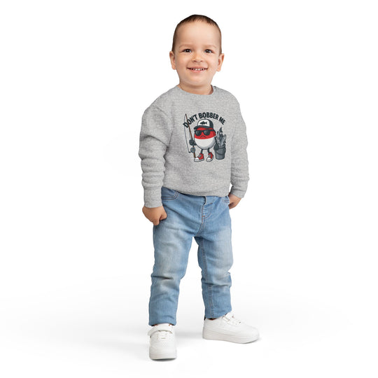 Toddler in light-wash jeans and white sneakers wearing a gray Don't Bobber Me sweatshirt with cartoon fishing bobber design, showcasing humor and style.