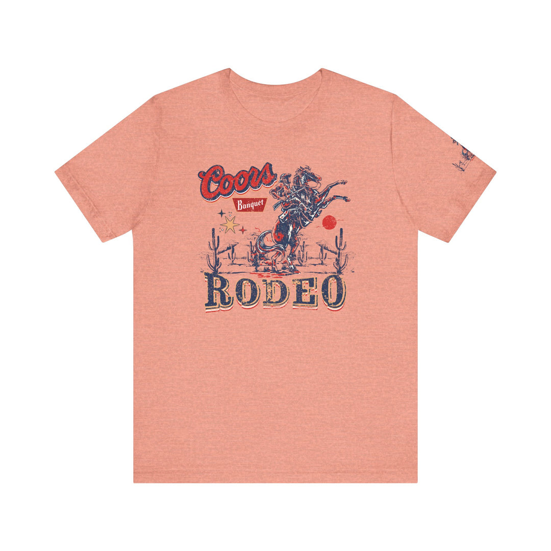 Coors Rodeo Tee: A pink t-shirt with a cowboy graphic design. Unisex jersey tee with ribbed knit collar, 100% cotton, retail fit, tear away label. Sizes XS-3XL.