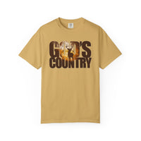 Mustard-colored God's Country Tee featuring a sunrise forest scene with a stag silhouette within the letters, reflecting a trendy, graphic design.
