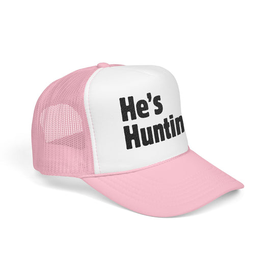 Pink and white mesh-back trucker cap with He's Huntin in bold black letters on the front, featuring a structured, high-profile design and adjustable snap.