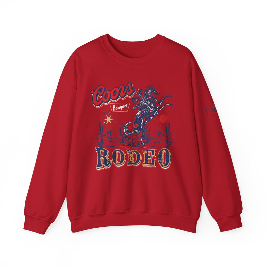 A red sweatshirt featuring a cowboy riding a horse graphic, the Coors Rodeo Crew. Unisex heavy blend, ribbed knit collar, 50% Cotton 50% Polyester, loose fit, medium-heavy fabric. Ideal comfort for any occasion.