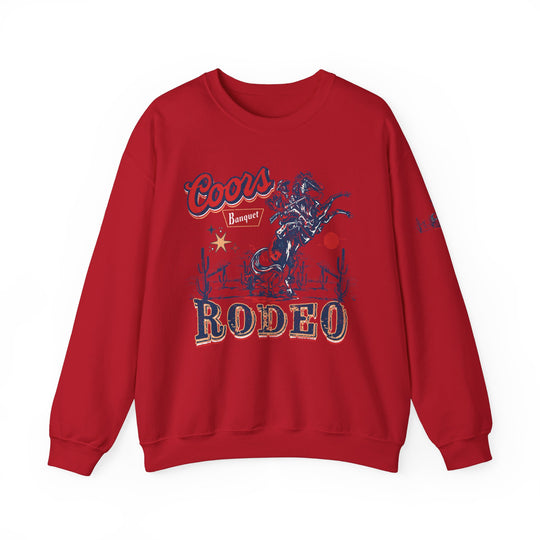 A red sweatshirt featuring a cowboy riding a horse graphic, the Coors Rodeo Crew. Unisex heavy blend, ribbed knit collar, 50% Cotton 50% Polyester, loose fit, medium-heavy fabric. Ideal comfort for any occasion.