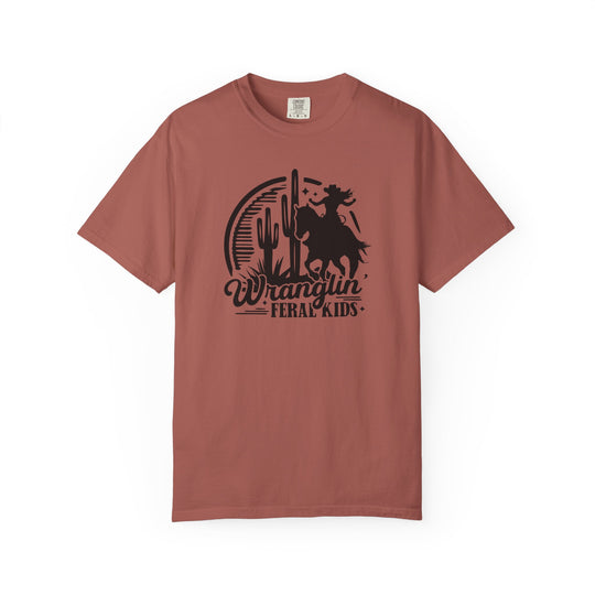 Wranglin Feral Kids Tee: Rust-colored crew-neck T-shirt featuring a cowboy silhouette, desert scene, and bold typography. Comfortable, durable, garment-dyed cotton for everyday wear.