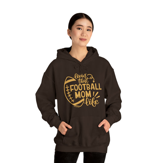 A brown Football Mom Life Hoodie with a football design, featuring a person wearing the hoodie with a football graphic, showcasing a classic fit and medium weight fabric. Ideal for casual fashion enthusiasts.