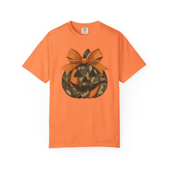 Jackie O Tee features a jack-o’-lantern with orange and camouflage segments, topped with an orange bow, on an orange short-sleeve T-shirt.