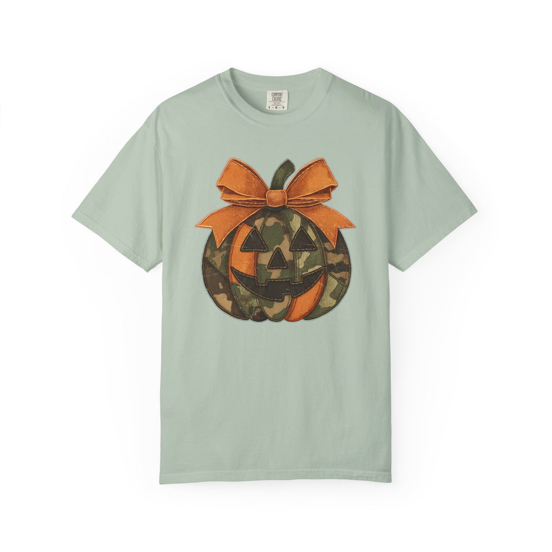 Jackie O Tee: Mint cotton T-shirt featuring a unique jack-o’-lantern graphic with orange and camouflage segments, adorned with an oversized orange bow.
