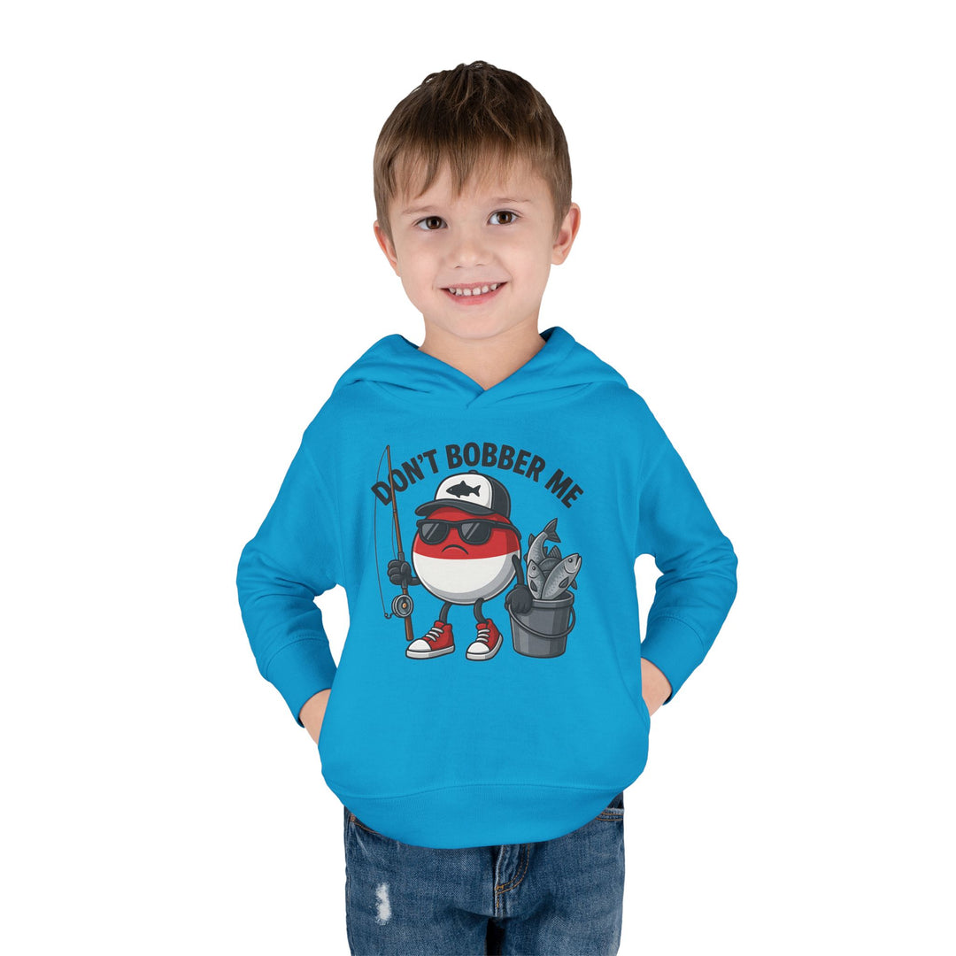 Young boy models the Don't Bobber Me Toddler Hoodie, featuring a cartoon bobber with fishing gear and a playful pun, designed for comfort and durability.