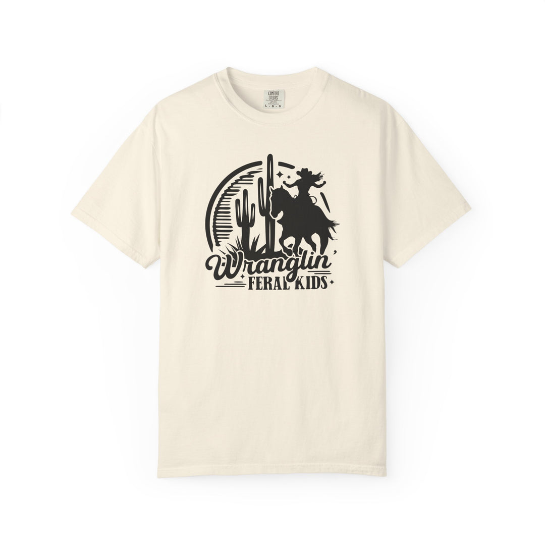 Cream-colored Wranglin’ Feral Kids T-shirt by Comfort Colors, featuring a black graphic of a figure on a bucking horse against a desert backdrop.