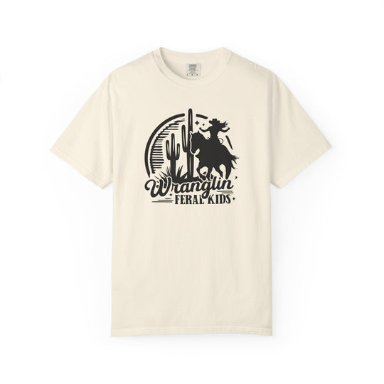 Cream-colored Wranglin’ Feral Kids T-shirt by Comfort Colors, featuring a black graphic of a figure on a bucking horse against a desert backdrop.