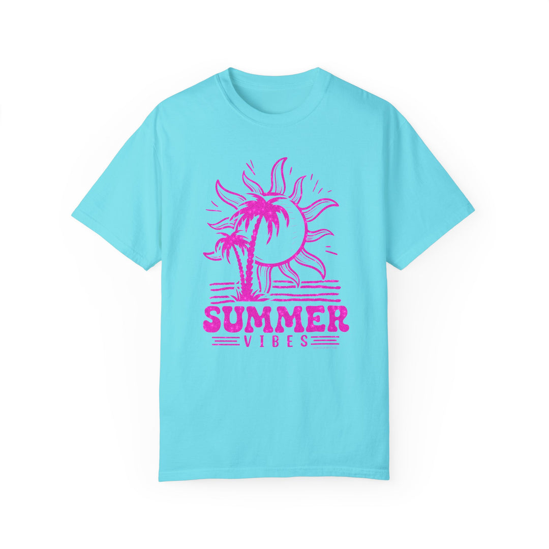 A garment-dyed Summer Vibes Tee in 100% ring-spun cotton, featuring a pink sun and palm trees design on a blue shirt. Relaxed fit, double-needle stitching, and seamless sides for durability and comfort.