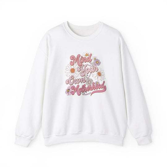 A white crewneck sweatshirt with pink text and floral designs, ideal for comfort in any situation. Unisex Mind Your Own Motherhood Crew made of 50% cotton, 50% polyester blend, ribbed knit collar, and no itchy side seams.