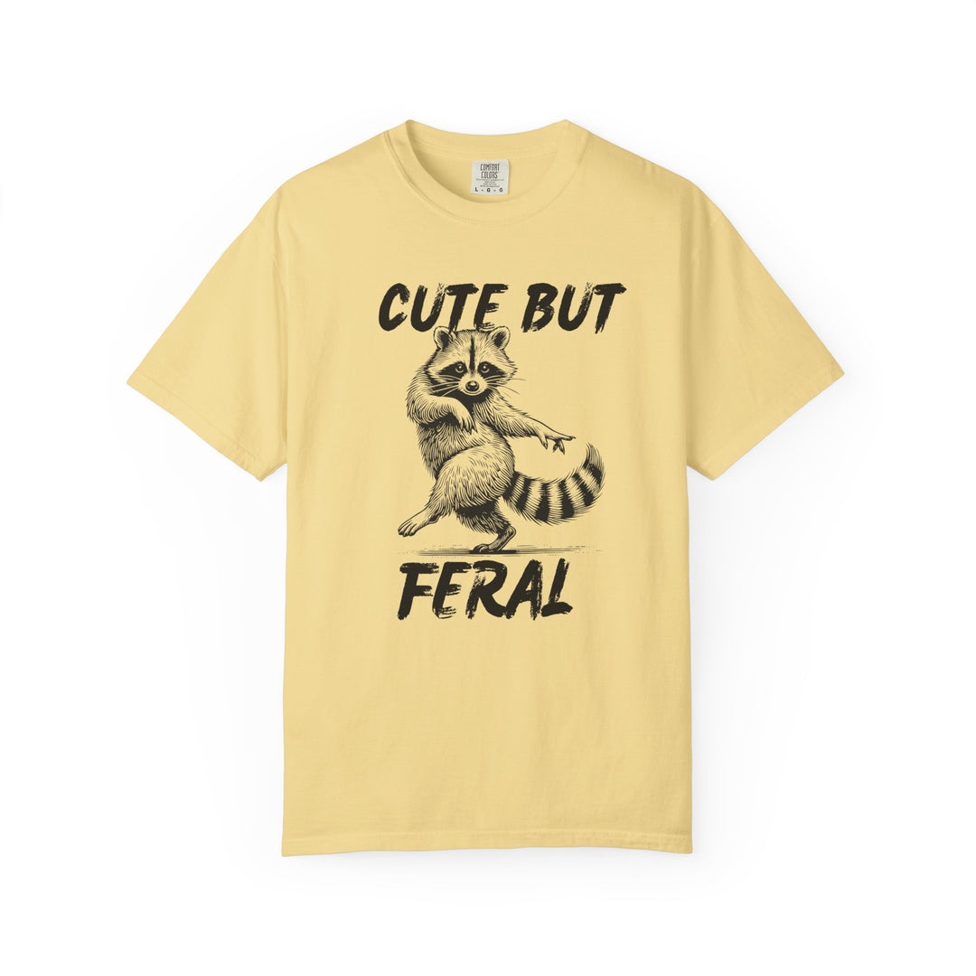 Cute but Feral Tee: Light yellow T-shirt featuring a dancing raccoon with CUTE BUT FERAL slogan, embodying comfort and humor with its relaxed fit and durable design.