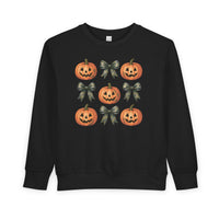 Pumpkins and Bows Toddler Crew: Black sweatshirt featuring a 3×3 grid of Halloween-themed jack-o’-lanterns and camouflage-pattern bows, designed for warmth and durability.