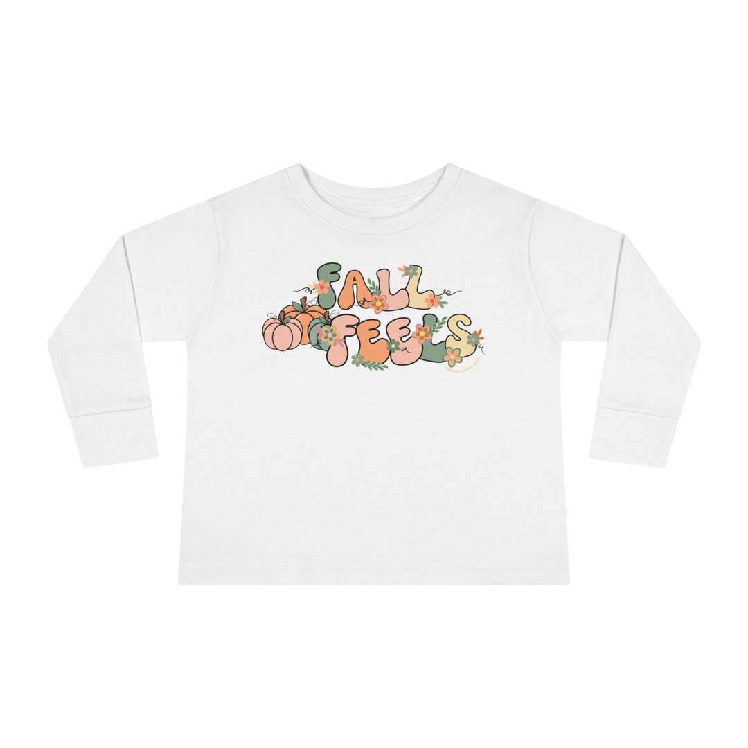 A custom Fall Feels Toddler Long Sleeve Tee in white, featuring a graphic design with words, flowers, and playful elements. Made of 100% combed ringspun cotton for durability and comfort.