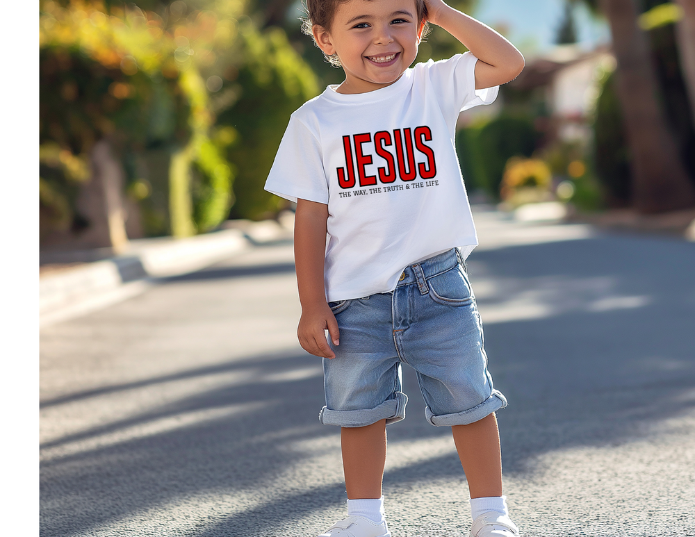 Young boy in a Jesus the Way, the Truth, the Life kids tee, smiling on a sunny street, showcasing the comfortable, durable cotton design for active wear.