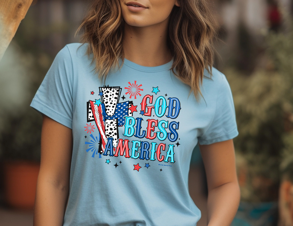 A woman in a blue shirt, close-up of a sign, and a logo with a sunburst. Product: God Bless America Cross Tee, unisex jersey tee with ribbed knit collars, taping on shoulders, and 100% Airlume combed cotton.