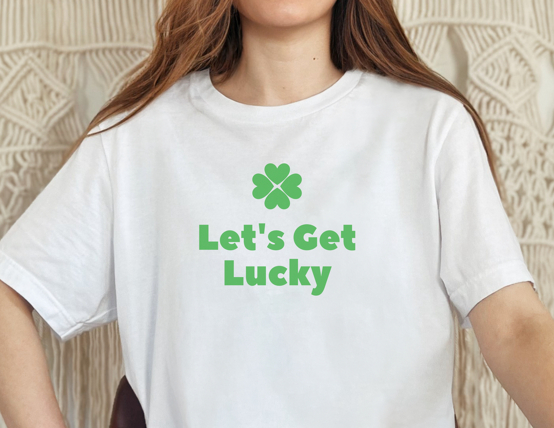 A woman in a Let's Get Lucky Tee, a white shirt with green text. Unisex heavy cotton tee with no side seams, tape on shoulders for durability, and ribbed knit collar. Classic fit, 100% cotton.