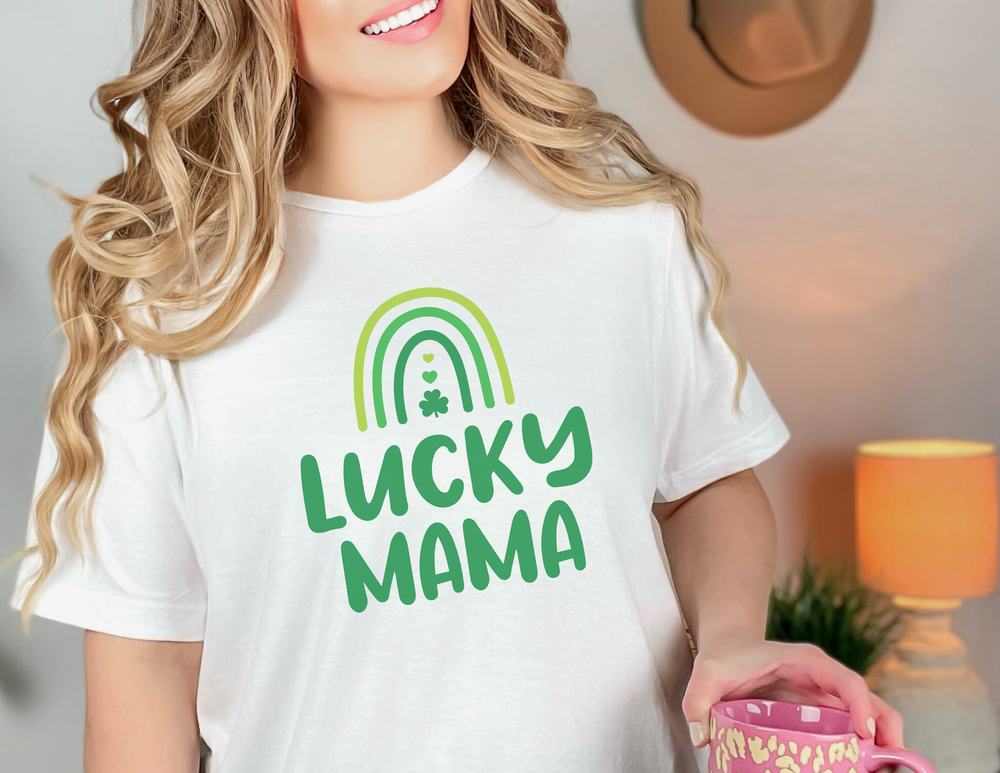 A woman in a white shirt holding a mug, showcasing the Mama Lucky Tee. Unisex jersey tee with ribbed knit collars, taping on shoulders, and Airlume combed cotton fabric. Retail fit, sizes XS to 3XL.