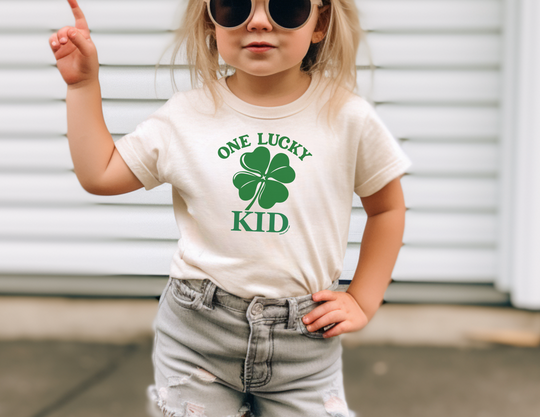 A girl in sunglasses and a t-shirt, showcasing the One Lucky Kid Tee from Worlds Worst Tees. Made of 100% US cotton, featuring durable twill tape shoulders and a classic fit for everyday comfort.