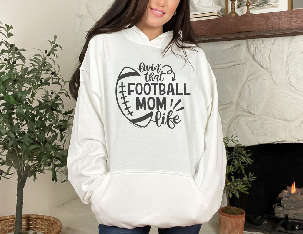 A white hoodie with a football design, perfect for Football Mom Life enthusiasts. Unisex heavy cotton tee with ribbed knit collar, tape on shoulders, and no side seams for comfort. Sizes from S to 5XL.