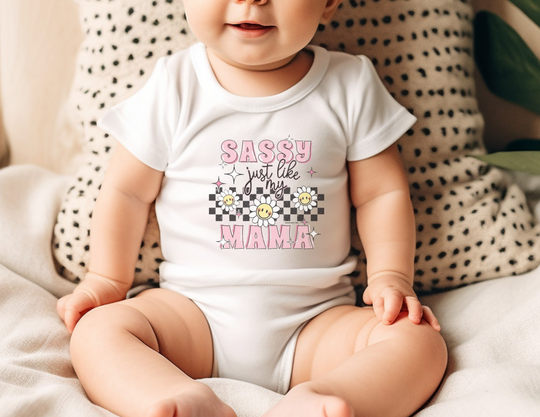 A baby wearing a Sassy like my mama onesie, sitting on a blanket. Infant fine jersey bodysuit, 100% cotton fabric, ribbed knitting for durability, plastic snaps for easy changing access. From Worlds Worst Tees.