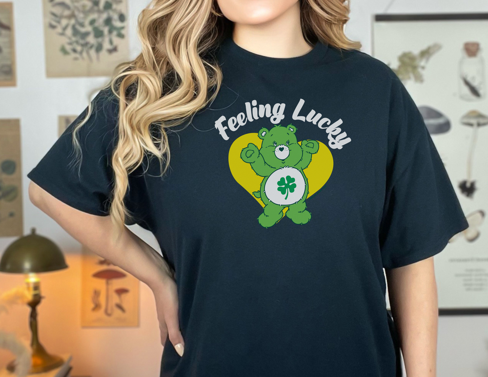 A woman in a Feeling Lucky Tee with a bear and clover design. Unisex heavy cotton tee with no side seams, tape on shoulders for durability, and ribbed knit collar. Classic fit, 100% cotton.