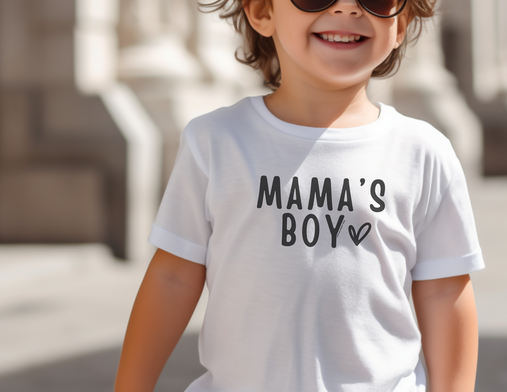 A child in sunglasses and a white tee smiles. Mama's Boy Toddler Tee: 100% cotton, 5.3 oz/yd², classic fit. Sizes 2T-6T. Width: 11.00-15.00 in, Length: 15.00-19.00 in, Sleeve: 9.00-12.50 in.