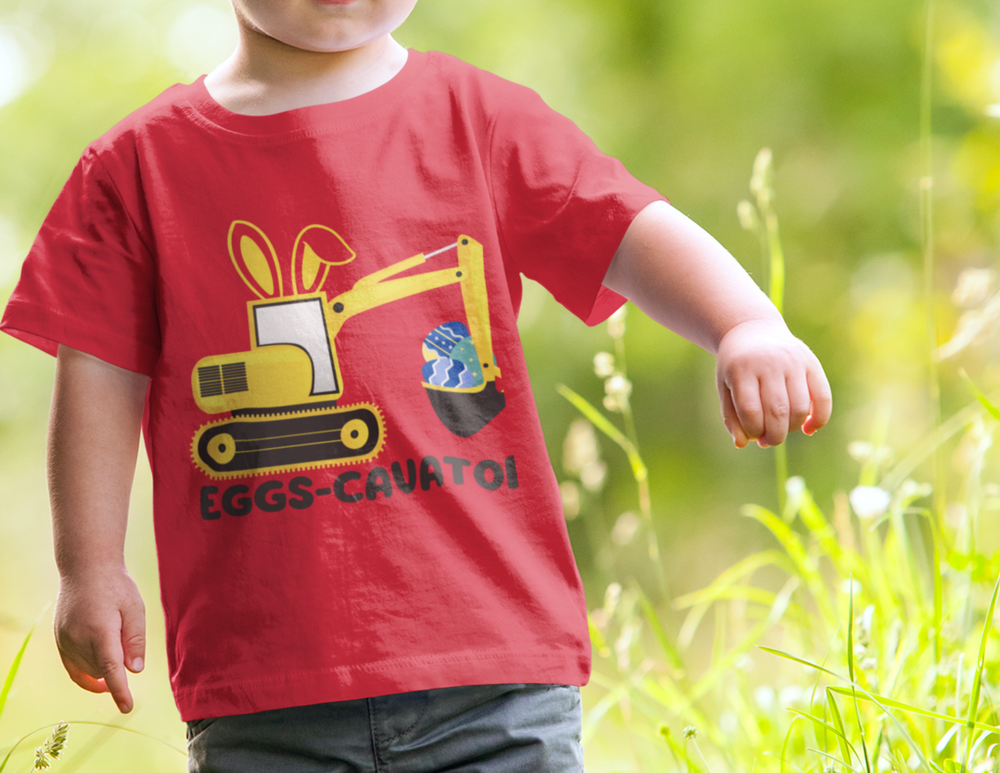 A toddler tee featuring an Eggs-Cavator design, with a red shirt worn by a child. Made of 100% ringspun cotton, with a classic fit and durable double-needle stitching. Ideal for active kids.