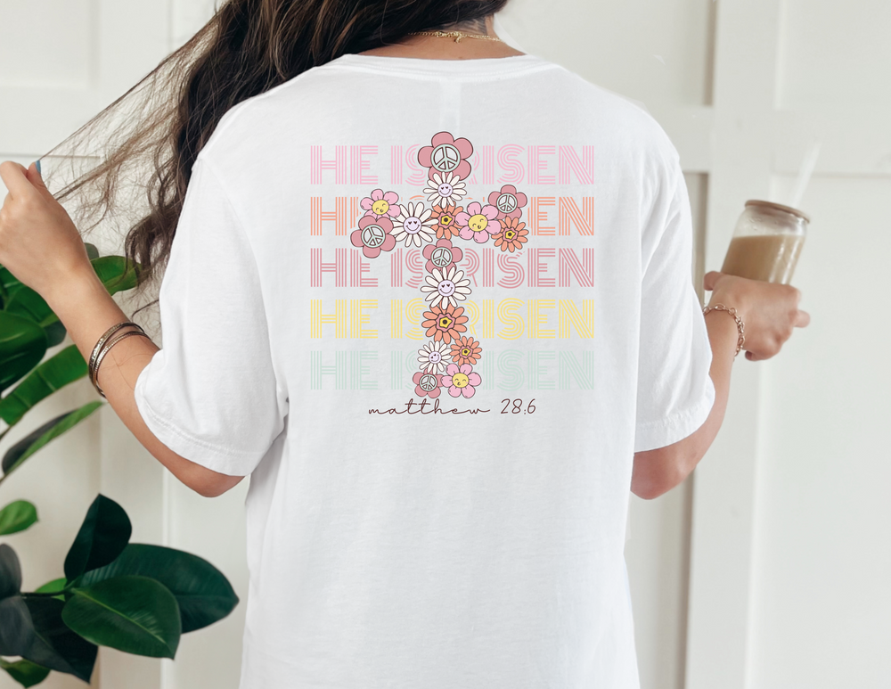 A relaxed fit He is Risen Easter Tee in white, featuring a cross design, made of 100% ring-spun cotton for comfort and durability. No side-seams for a tubular shape.