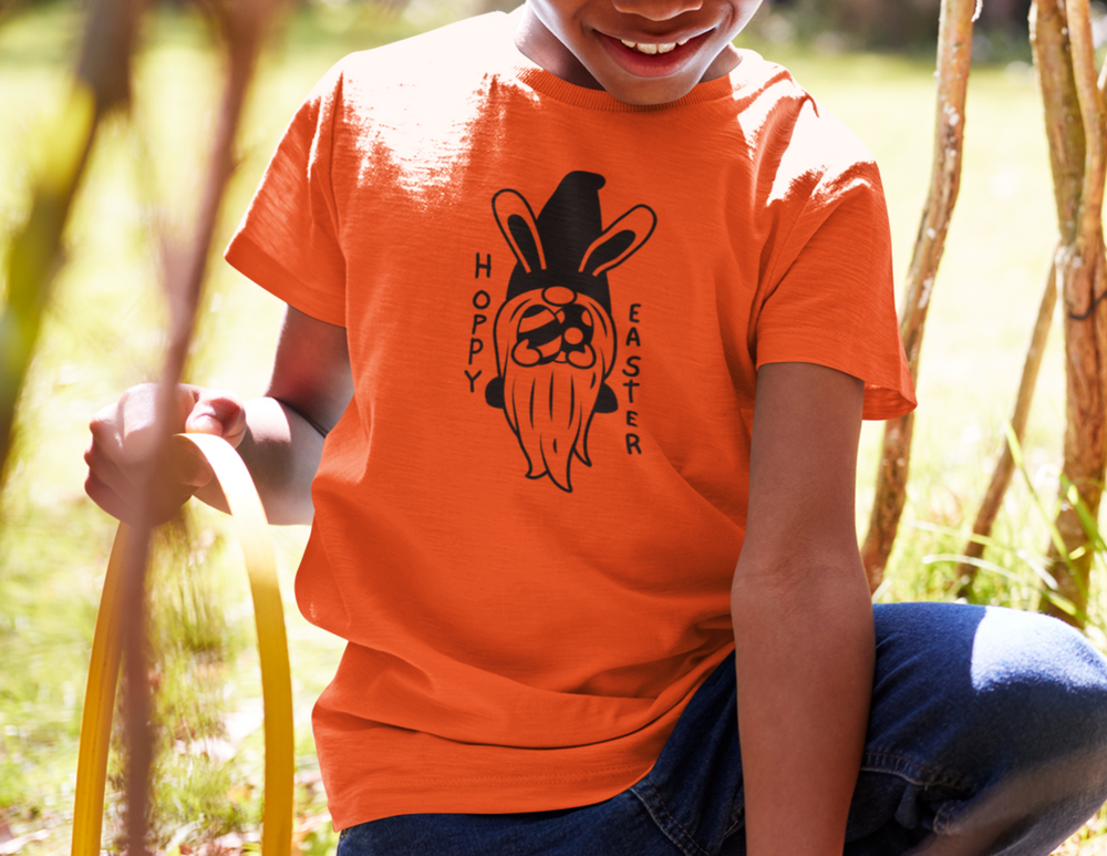 Hoppy Easter Toddler Tee: A 100% Airlume cotton jersey tee for toddlers featuring a boy in an orange shirt holding a strap. Perfect for comfort and style.