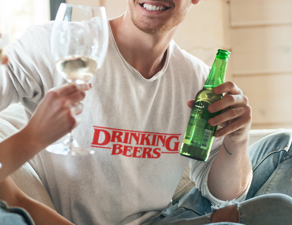 A man holding a bottle of beer, embodying the DRINKING BEERS tee's relaxed vibe. Crafted from 100% ring-spun cotton for coziness and durability. Perfect for daily wear with a soft-washed finish.