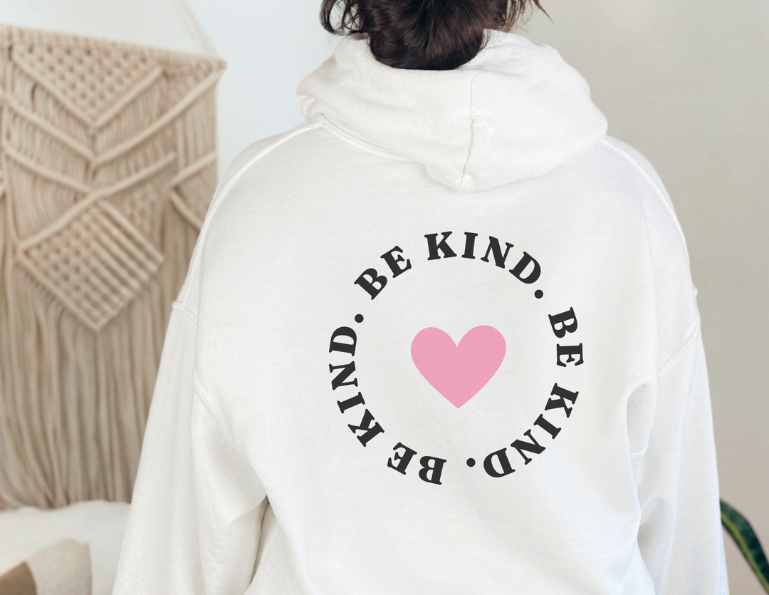 Unisex BE KIND Sweatshirt: White with pink heart design. Heavy blend fabric, kangaroo pocket, matching drawstring hood. Cozy, stylish, perfect for cold days. Classic fit, tear-away label, true to size.