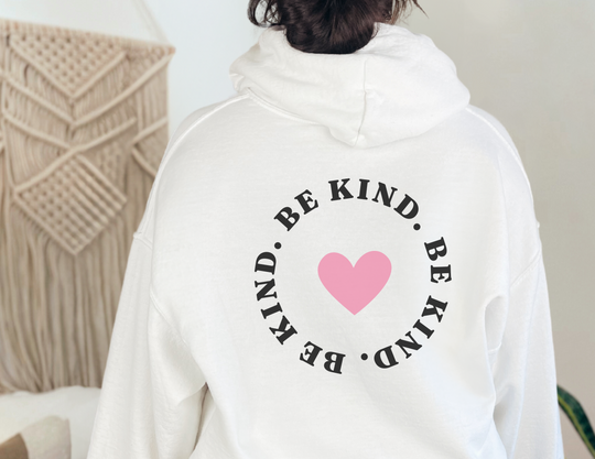 Unisex BE KIND Sweatshirt: White with pink heart design. Heavy blend fabric, kangaroo pocket, matching drawstring hood. Cozy, stylish, perfect for cold days. Classic fit, tear-away label, true to size.
