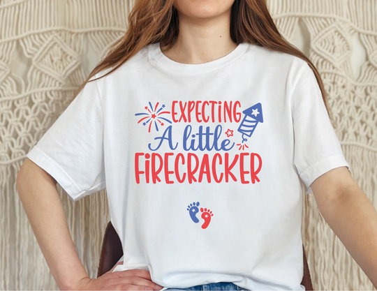 A white tee featuring a playful design of red and blue footprints, stars, and fireworks. Unisex heavy cotton fabric with no side seams, tape on shoulders, and ribbed knit collar for comfort and durability.