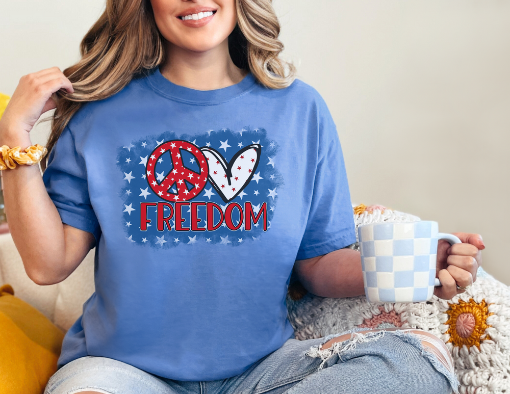 A woman in a relaxed fit Love Freedom Garment Dyed Tee, holding a mug. Made of 100% ring-spun cotton for coziness and durability. No side-seams for a tubular shape.