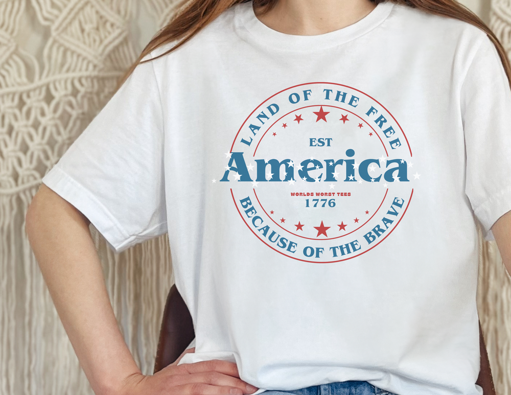 Unisex America Land of the Free Tee, featuring a person in a white shirt with red and blue logos. Made of 100% cotton, retail fit, with ribbed knit collars and taping on shoulders for a comfortable, lasting wear.