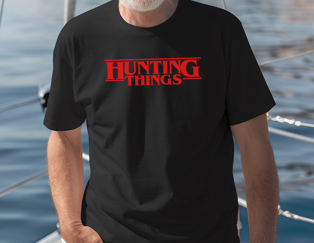 A relaxed fit HUNTING THINGS tee in black, featuring a man in a black shirt by the lake. Made of 100% ring-spun cotton for coziness and durability, perfect for daily wear.