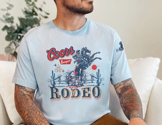 A classic Coors Rodeo Tee for all, featuring a man in a white shirt with a cowboy design. Unisex jersey tee made of 100% Airlume combed cotton, with ribbed knit collars and taping on shoulders for lasting comfort and fit.