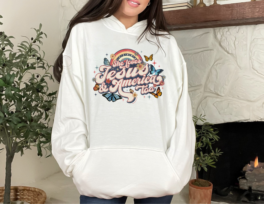 A white hoodie with a graphic design featuring butterflies and flowers, ideal for relaxation. Unisex heavy blend, cotton-polyester fabric, kangaroo pocket, and drawstring hood. Product title: She Loves Jesus and America Hoodie.