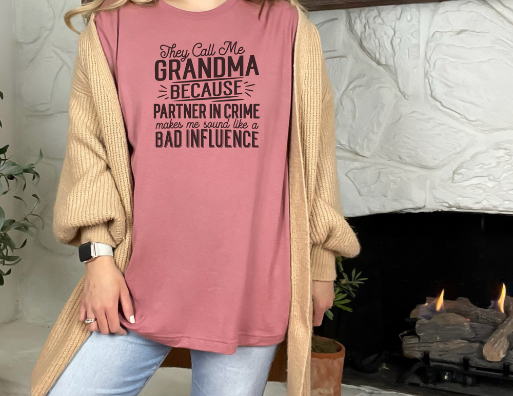 A relaxed fit They Call Me Grandma Tee, made of 100% ring-spun cotton, featuring a close-up of a woman in a pink shirt posing. Garment-dyed for extra coziness, with double-needle stitching for durability.