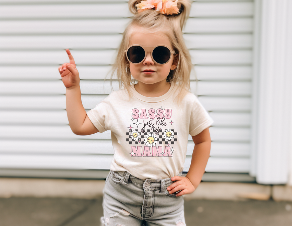 Toddler tee featuring a girl with sunglasses and a bow, embodying sass like mama. Made of 100% cotton for softness, with a rib collar for style and comfort. Classic fit in sizes 2T to 6T.