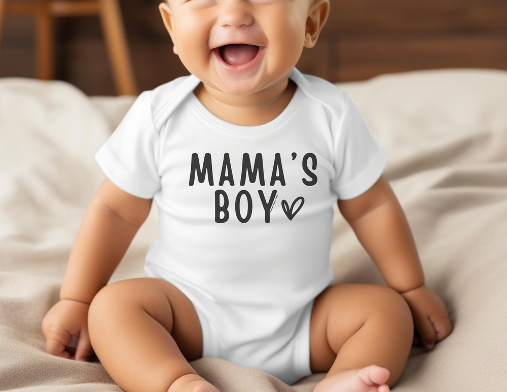 A baby boy in a Mama's Boy Onesie, smiling and sitting on a blanket. The infant fine jersey bodysuit is 100% cotton, featuring ribbed knitting for durability and plastic snaps for easy changing.