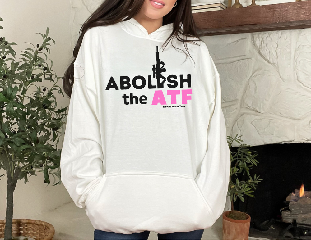 A woman in a white sweatshirt poses for a picture. Unisex Abolish the ATF Hoodie: cotton-polyester blend, cozy, kangaroo pocket, drawstring hood. From 'Worlds Worst Tees'.