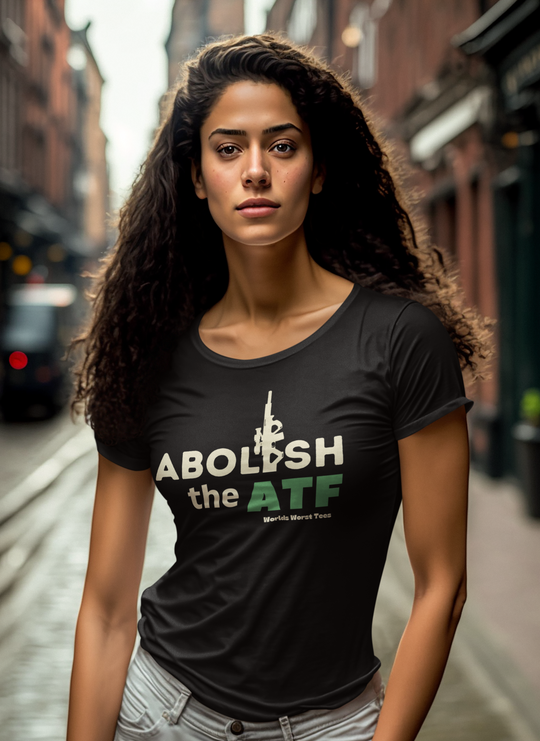 A woman in a black shirt with white text and a gun, emphasizing the Abolish the ATF Tee product from Worlds Worst Tees. Premium fitted men's short sleeve, light fabric, tear-away label, and a statement print.