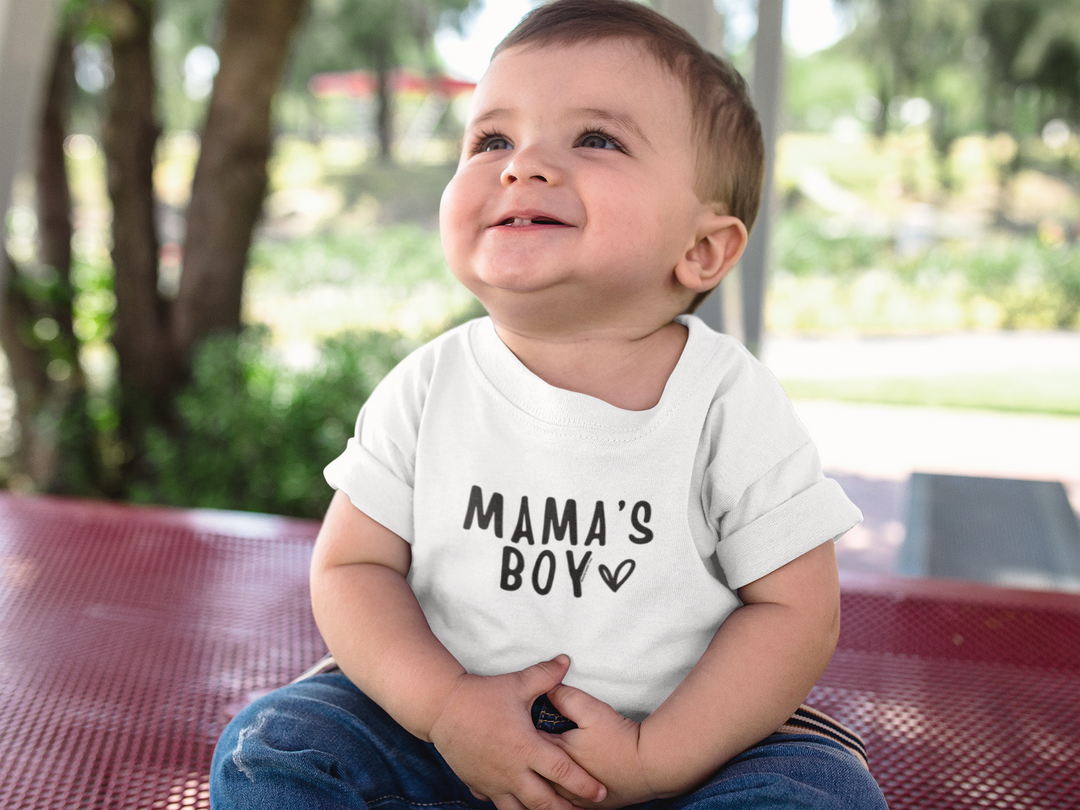 A toddler tee featuring Mama's Boy design, crafted from 100% cotton for softness. Classic fit with rib collar for comfort. Image shows a baby sitting on a bench.