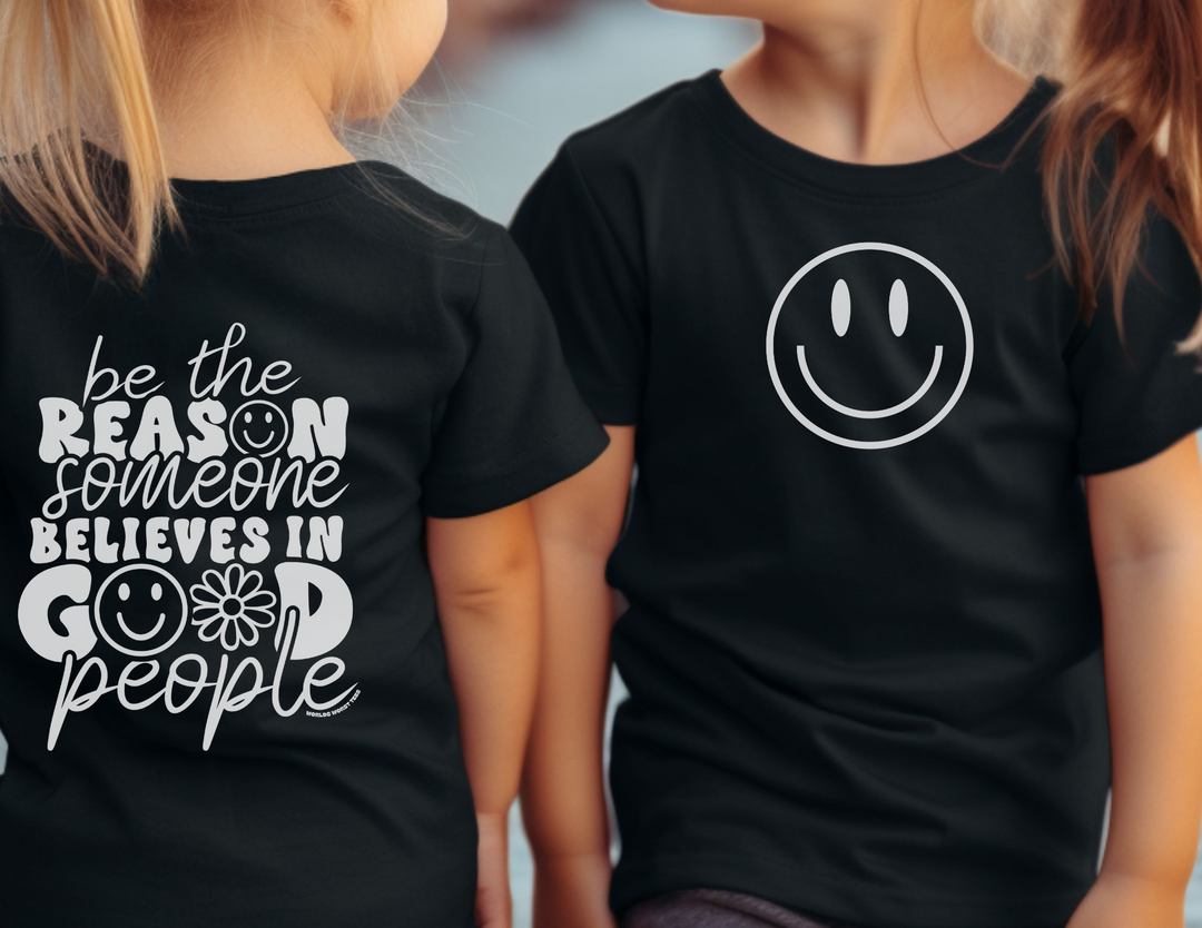 Two girls in black shirts, one with a smiley face, showcase the Be the Reason Kids Tee. A lightweight, custom youth shirt made of 100% cotton for comfort and style. Perfect for kids.