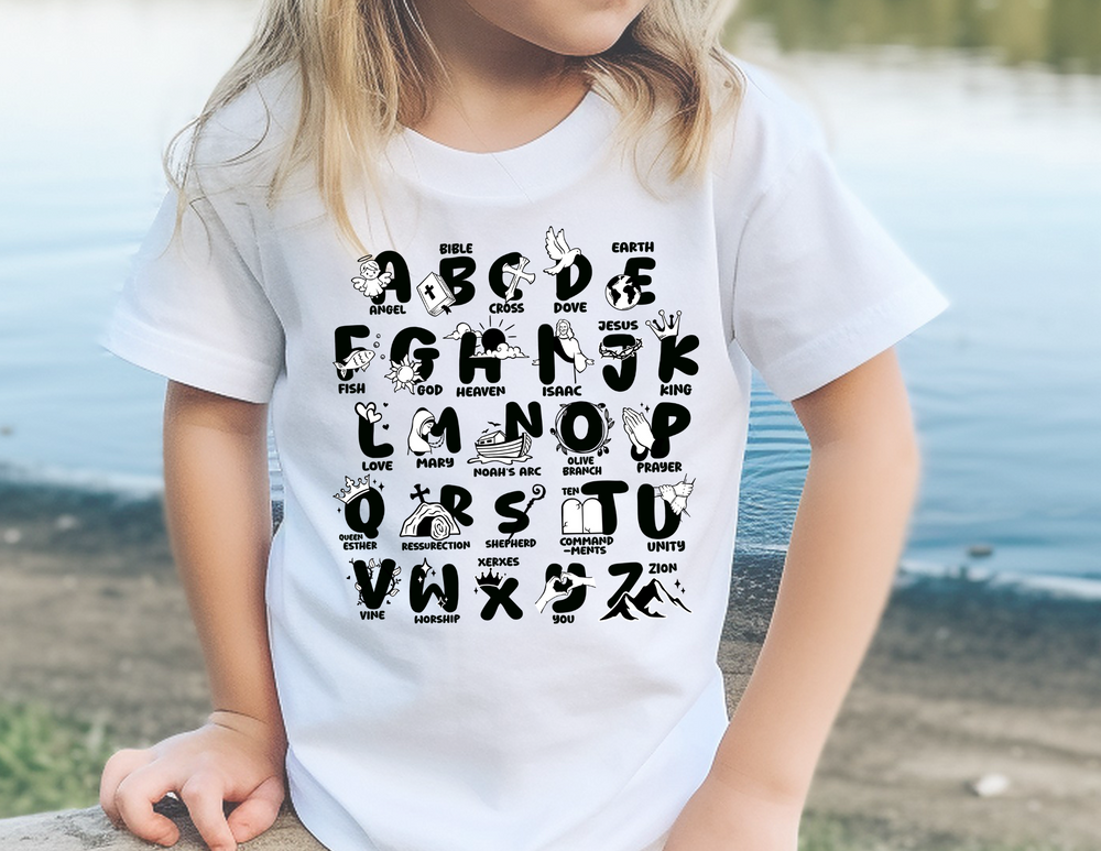 A Bible Alphabet Toddler Tee featuring a child near water, wearing a white shirt with alphabet letters. Made of 100% ringspun cotton, light fabric, tear-away label, perfect for sensitive skin. Ideal for first adventures.