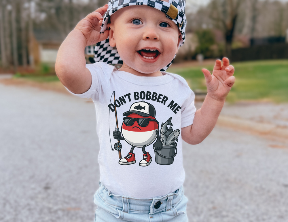 Toddler wearing Don't Bobber Me Baby Tee with a grumpy bobber graphic, standing on a paved surface, embodying playful style and comfort.