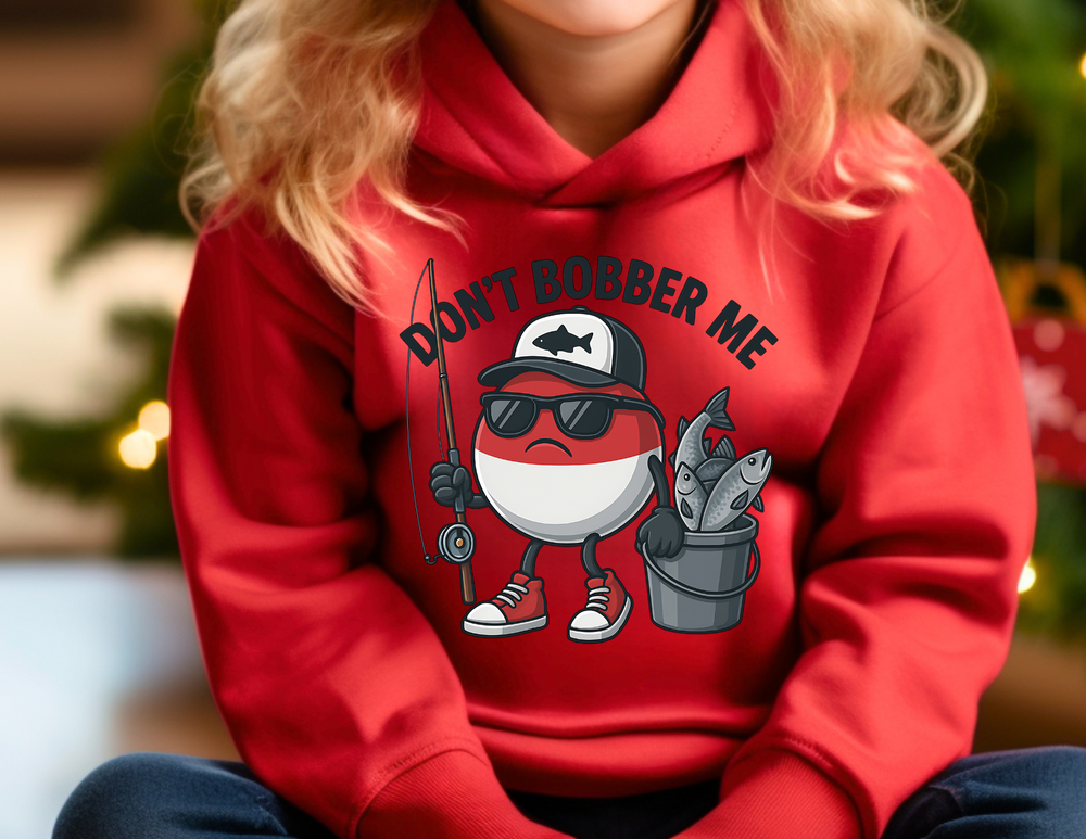 Child in a red Don't Bobber Me Youth Hoodie with cartoon bobber character. Cozy, ultra-soft fleece, kangaroo pocket, ideal for unique graphic hoodie lovers.